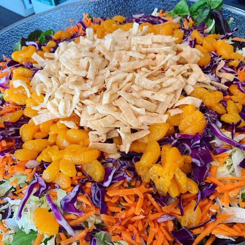 A wide serving platter of shredded salad — red cabbage, carrot, mandarin segments and crisp noodles piled in the center.